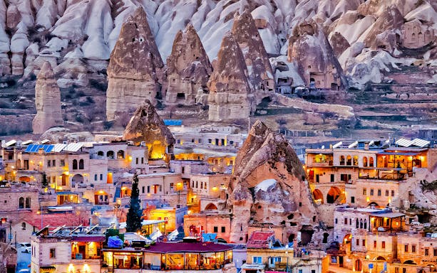 Cappadocia rock formations and illuminated cave dwellings at dusk.