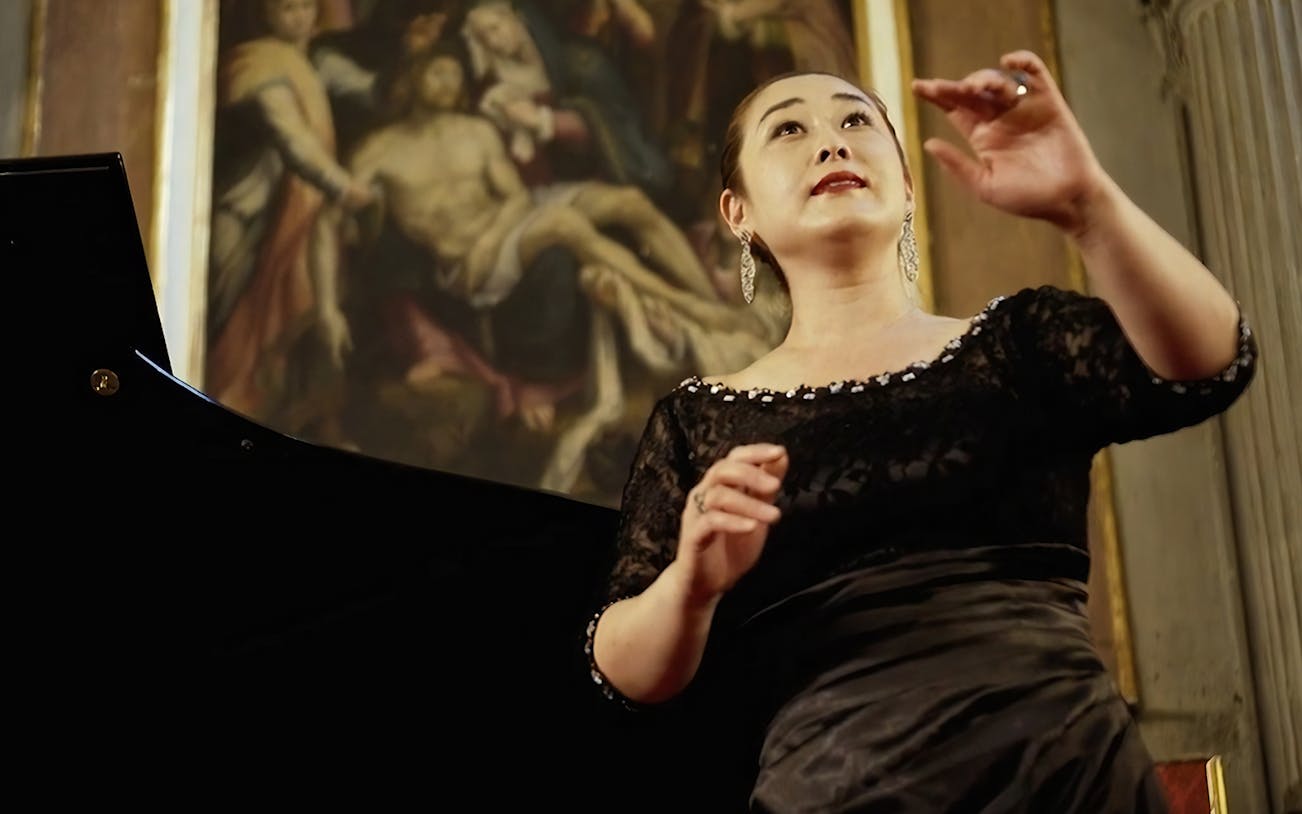 Opera singer performing at a concert in Florence with classical painting in the background.