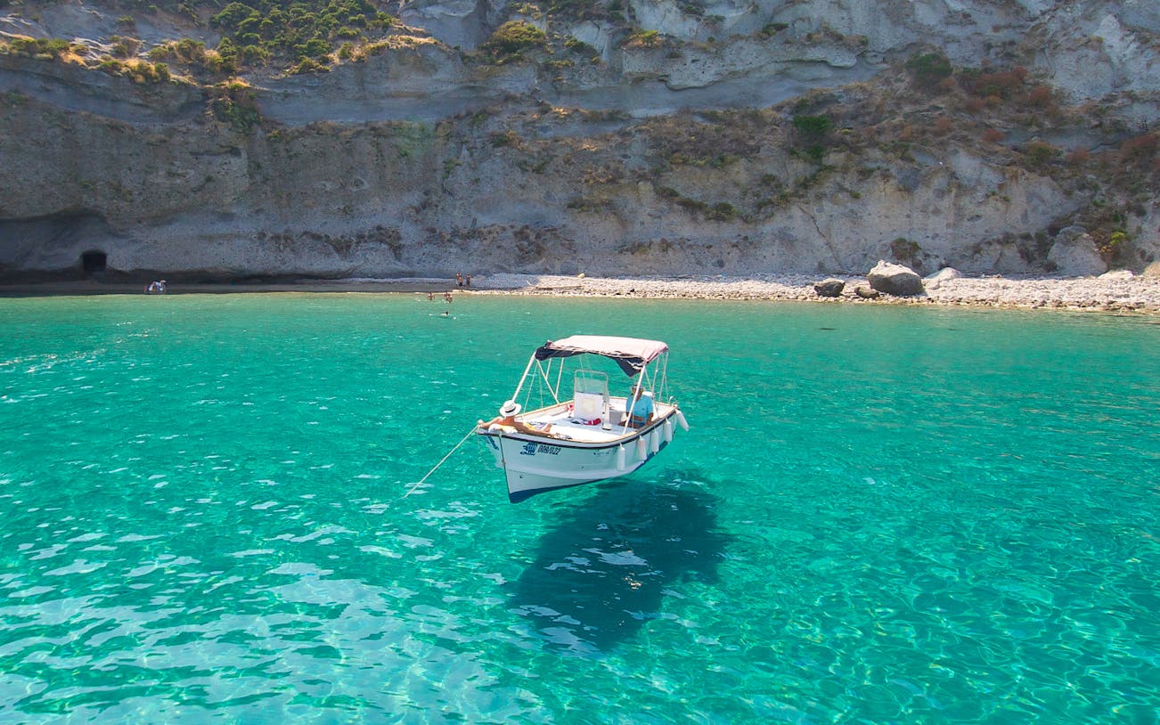 Boat anchored in clear waters near rocky shore on Ponza Island day trip from Rome.