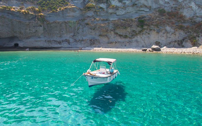 Boat anchored in clear waters near rocky shore on Ponza Island day trip from Rome.