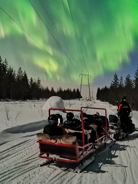 Snowmobile ride under Northern Lights in Levi, Finland.