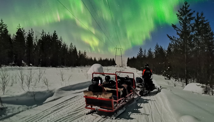 Snowmobile ride under Northern Lights in Levi, Finland.