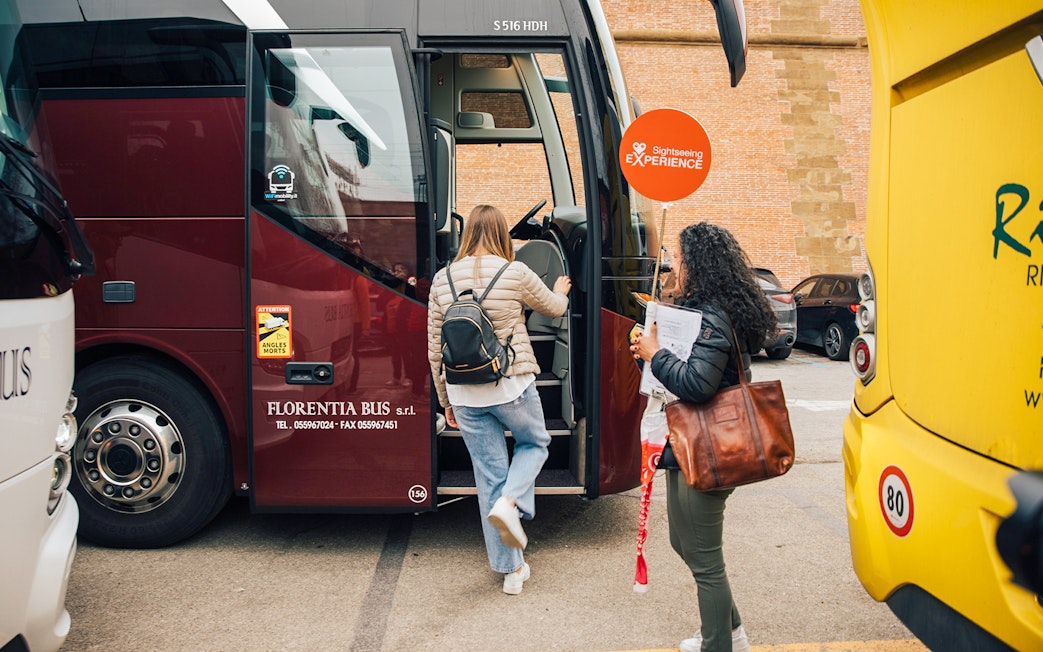 Tourists boarding a bus for the Tuscany in a Day tour, visiting Siena, San Gimignano, and Pisa.
