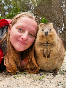 Person smiling with a quokka on Rottnest Island during a ferry and adventure boat tour.
