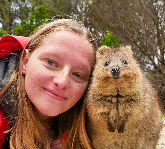 Person smiling with a quokka on Rottnest Island during a ferry and adventure boat tour.