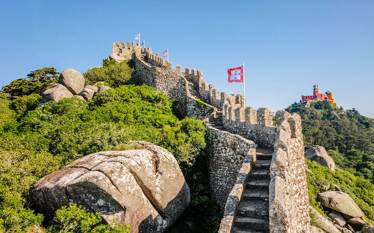 Moorish Castle ruins with steps and flags, Pena Palace in background, Sintra, Portugal.