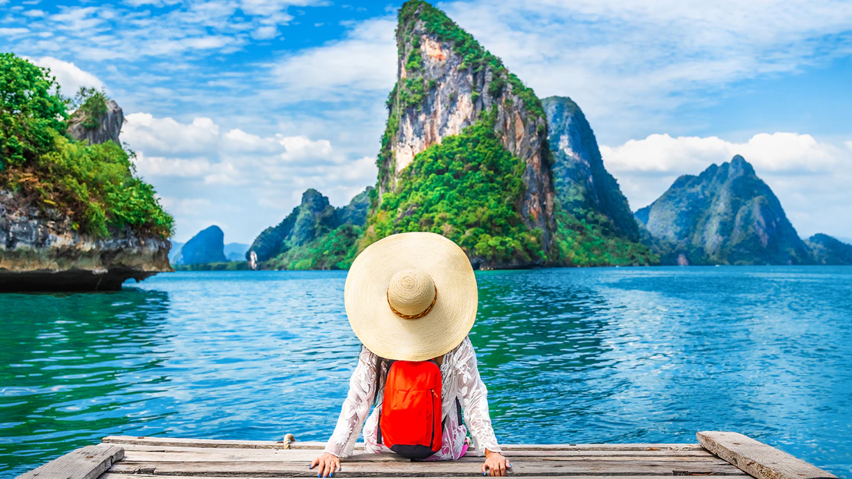 Canoeing tour participant on dock with view of Phang Nga Bay and limestone cliffs, Thailand.