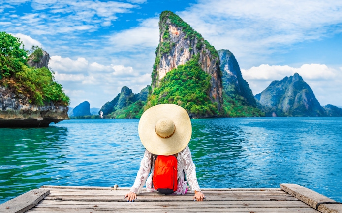 Canoeing tour participant on dock with view of Phang Nga Bay and limestone cliffs, Thailand.