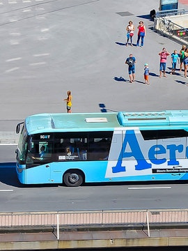 Aerobus driving on a city street with people waiting nearby.