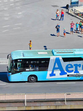 Aerobus driving on a city street with people waiting nearby.