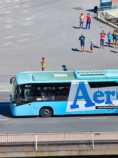 Aerobus driving on a city street with people waiting nearby.