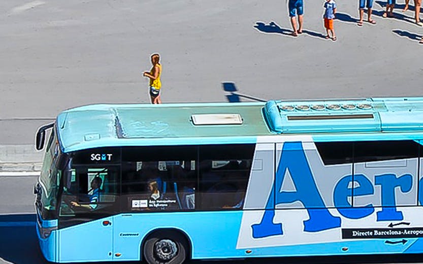 Aerobus driving on a city street with people waiting nearby.