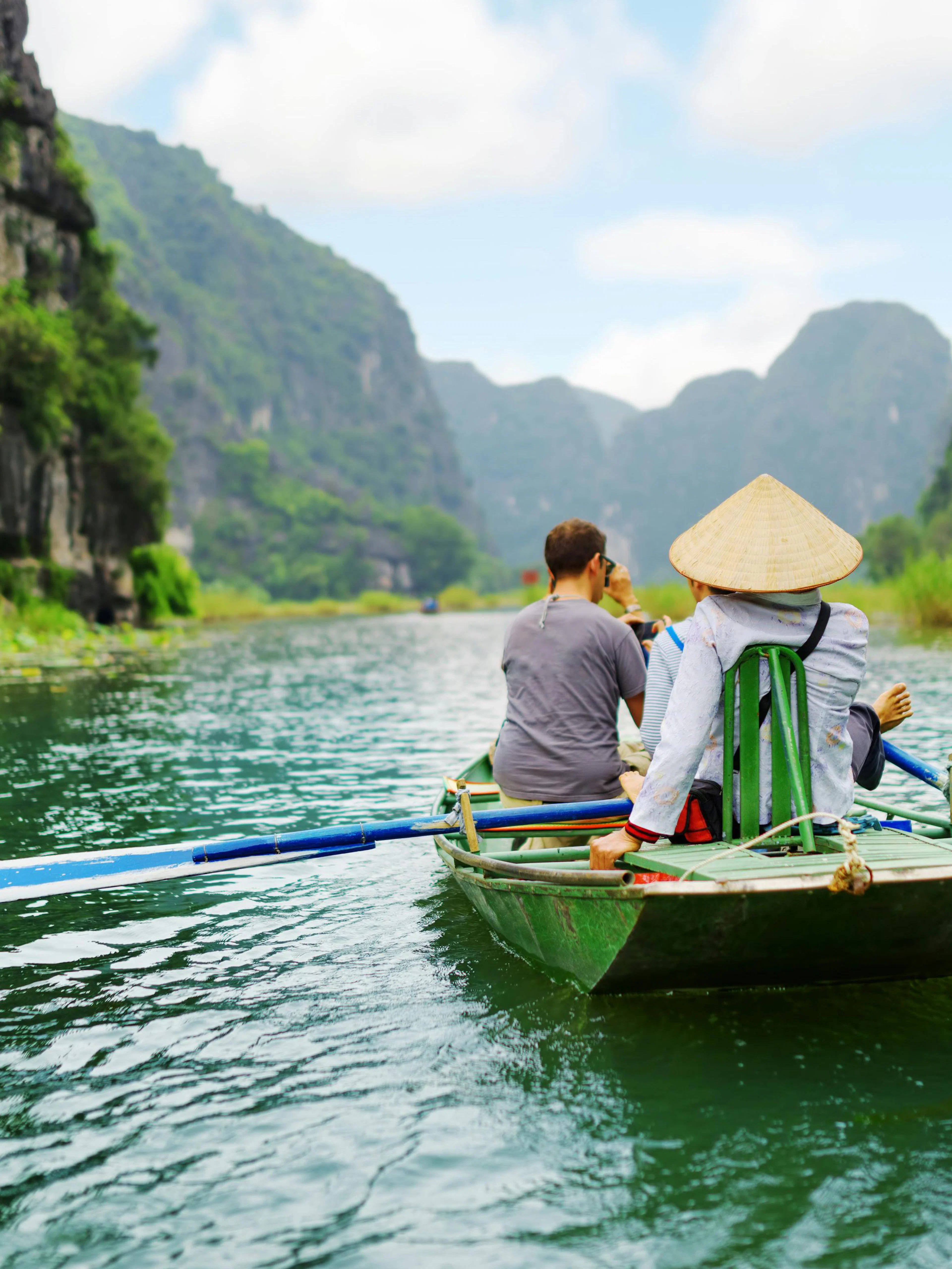 Tourists rowing boat through limestone cliffs at Tam Coc, Vietnam.