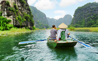 Tourists rowing boat through limestone cliffs at Tam Coc, Vietnam.