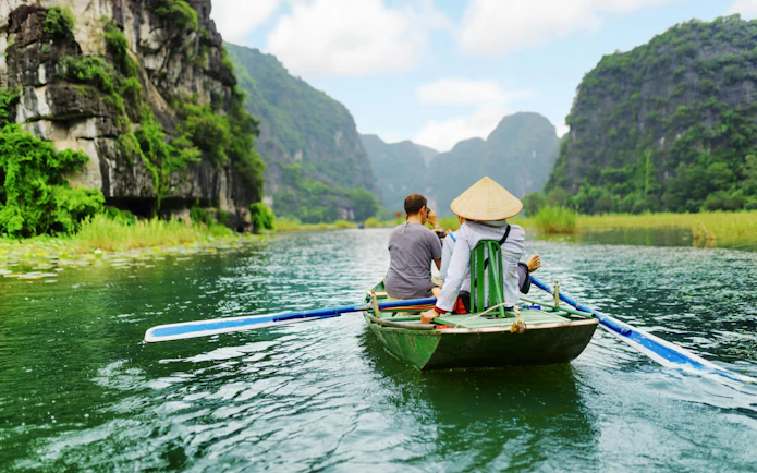 Tourists rowing boat through limestone cliffs at Tam Coc, Vietnam.