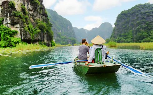 Tourists rowing boat through limestone cliffs at Tam Coc, Vietnam.