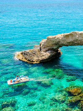 Pedal boat near Cyprus Bridge of Lovers over clear turquoise water.