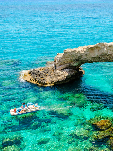 Pedal boat near Cyprus Bridge of Lovers over clear turquoise water.