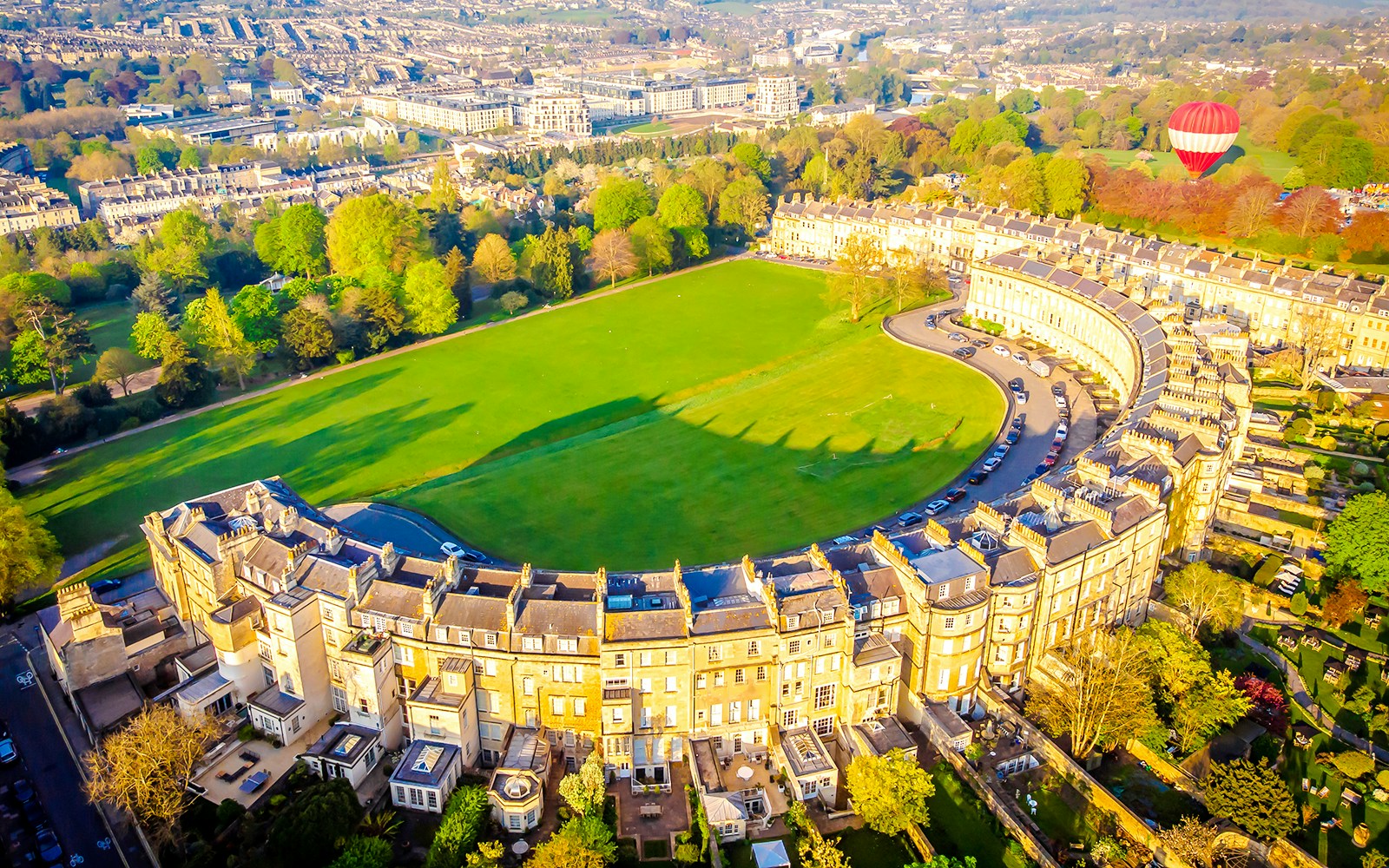 Aerial view of the Royal Crescent in Bath, UK, with a hot air balloon in the background.