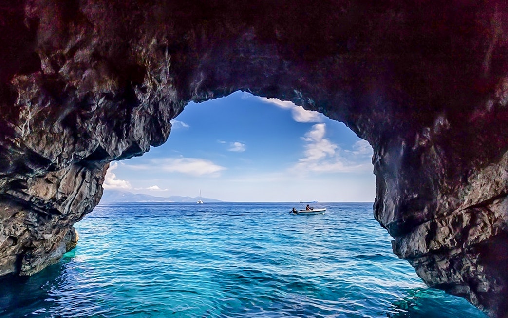 Boat approaching blue caves with rocky entrance and clear sea.