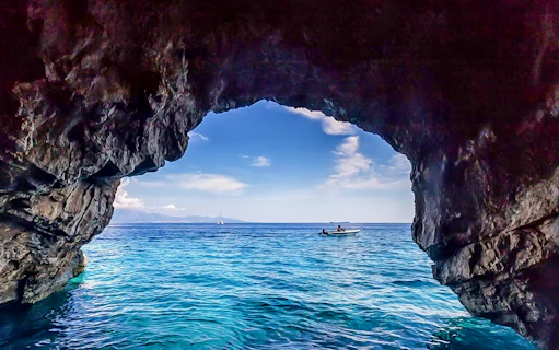 Boat approaching blue caves with rocky entrance and clear sea.