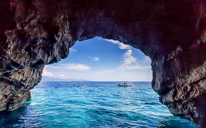 Boat approaching blue caves with rocky entrance and clear sea.