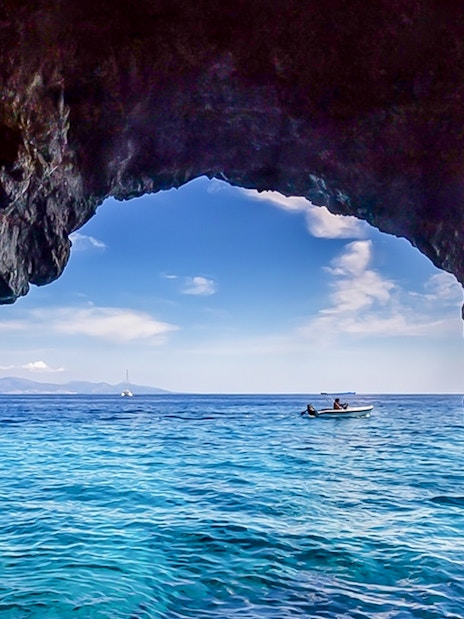 Boat approaching blue caves with rocky entrance and clear sea.