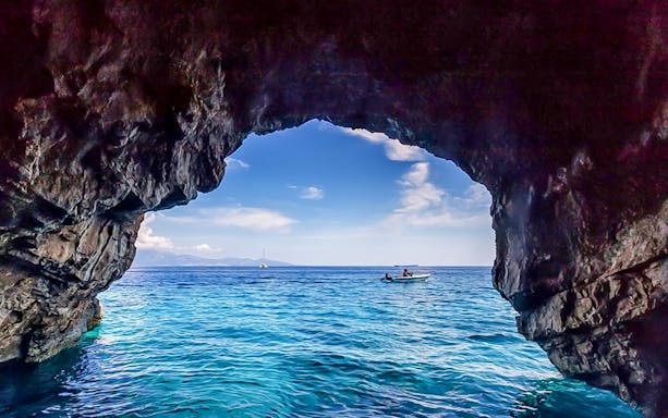 Boat approaching blue caves with rocky entrance and clear sea.