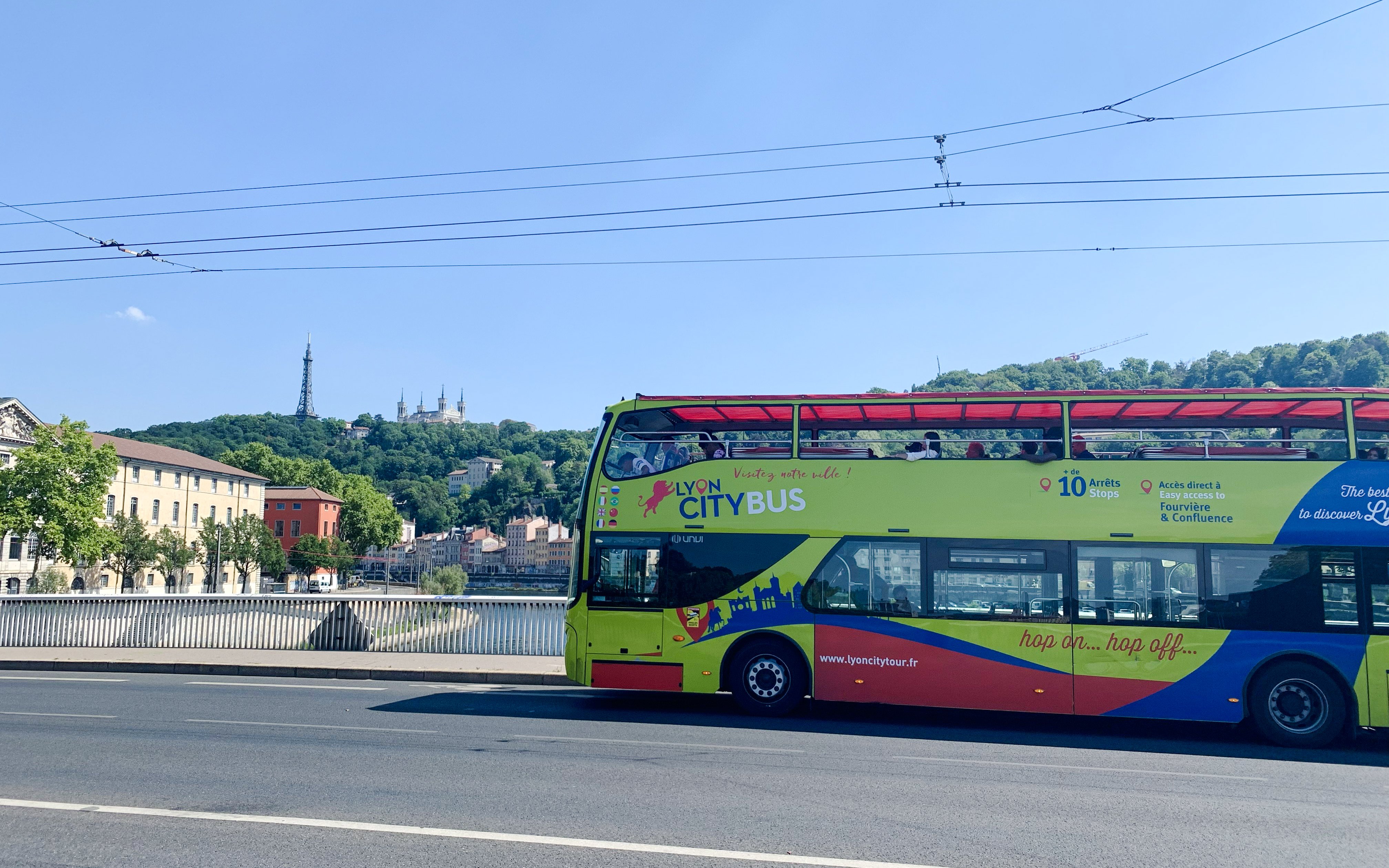 Lyon city tour bus on a bridge with Basilica of Notre-Dame de Fourvière in the background, France.