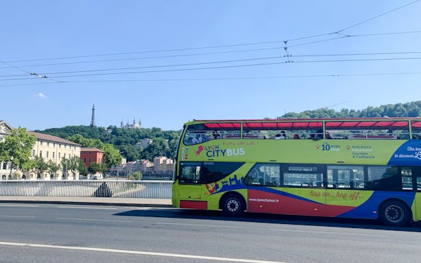 Lyon city tour bus on a bridge with Basilica of Notre-Dame de Fourvière in the background, France.