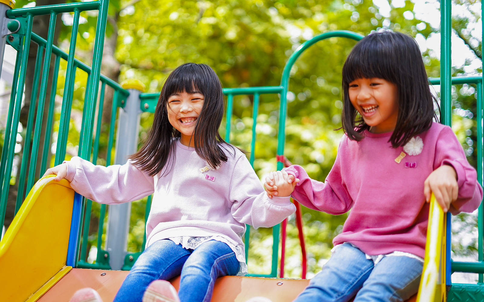 Children holding hands while sliding down a playground slide.
