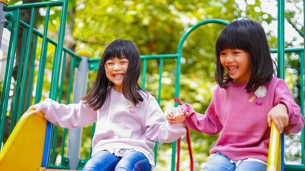 Children holding hands while sliding down a playground slide.