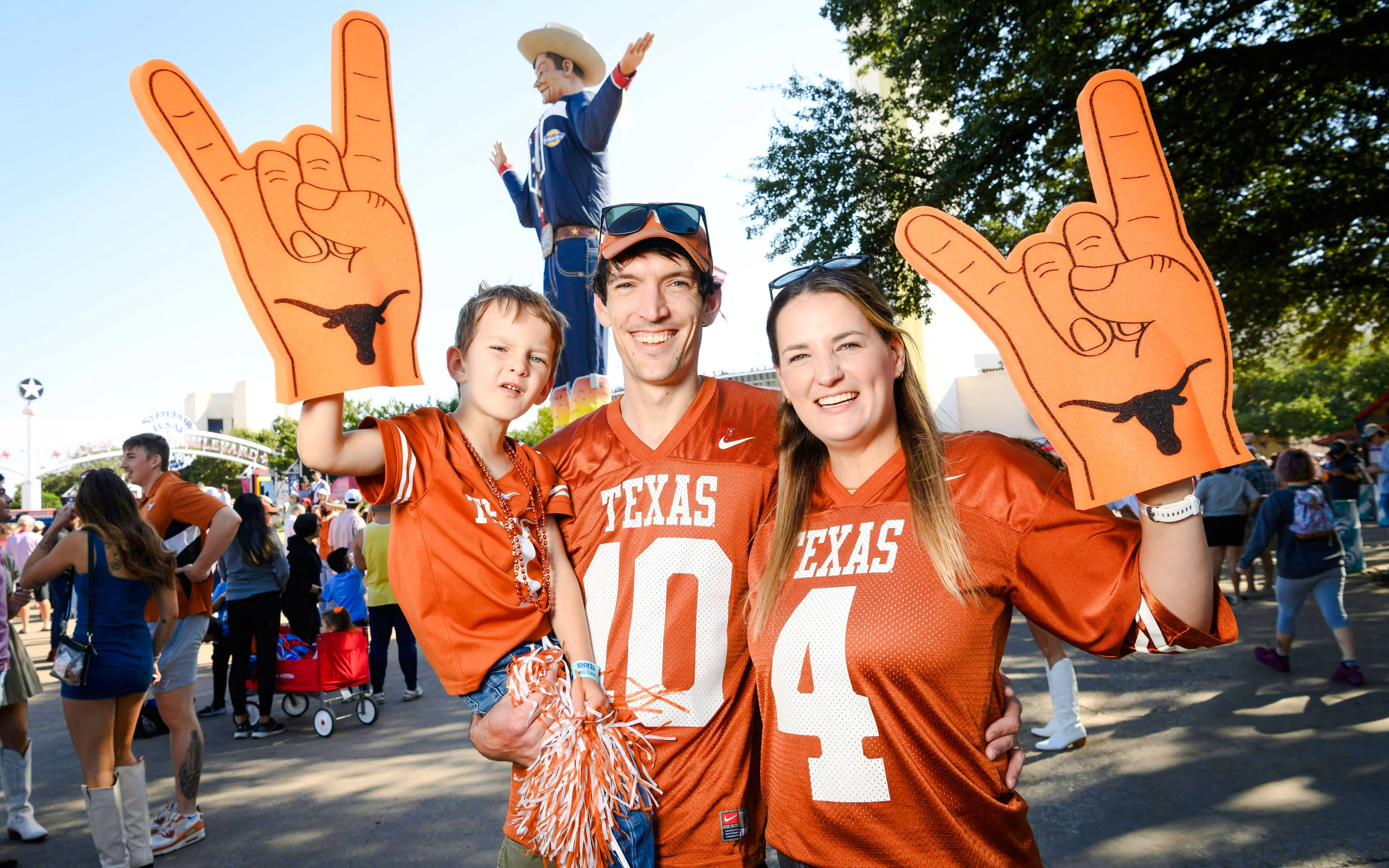Family in Texas jerseys at State Fair of Texas with Big Tex statue in background.
