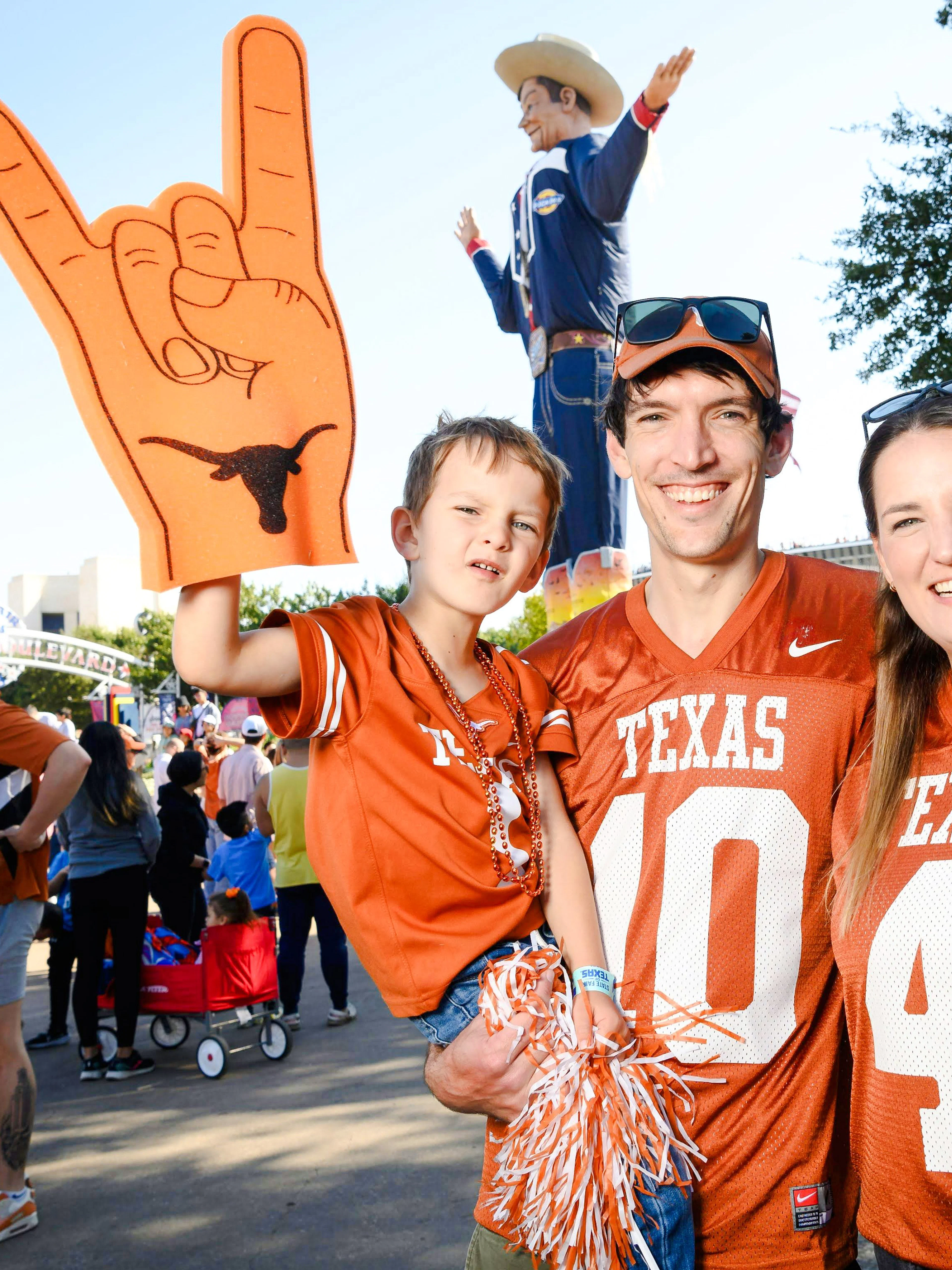 Family in Texas jerseys at State Fair of Texas with Big Tex statue in background.