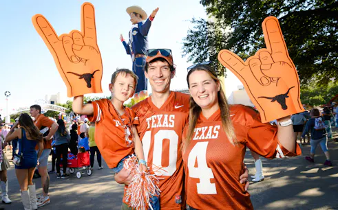 Family in Texas jerseys at State Fair of Texas with Big Tex statue in background.