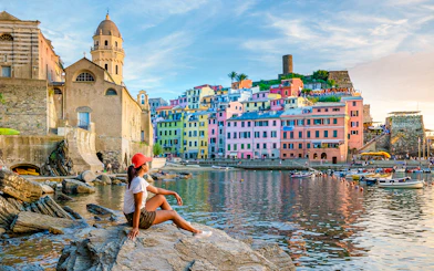 Tourist sitting on rocks overlooking colorful buildings in Vernazza, Cinque Terre.
