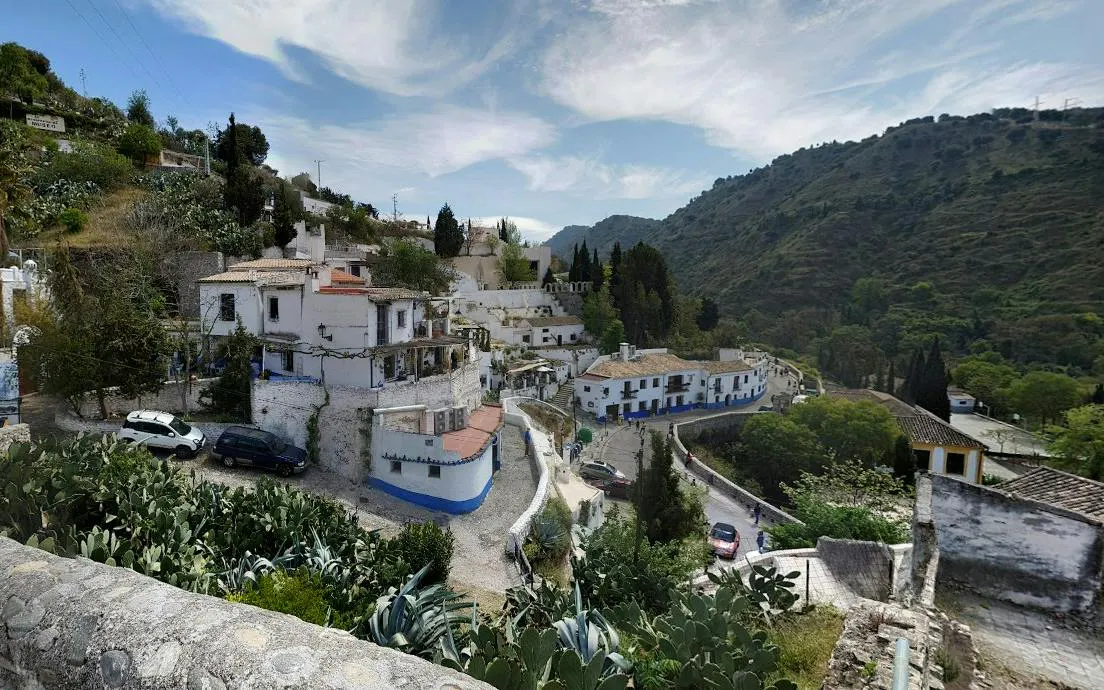 White hillside houses in Sacromonte, Granada, surrounded by greenery and mountains.