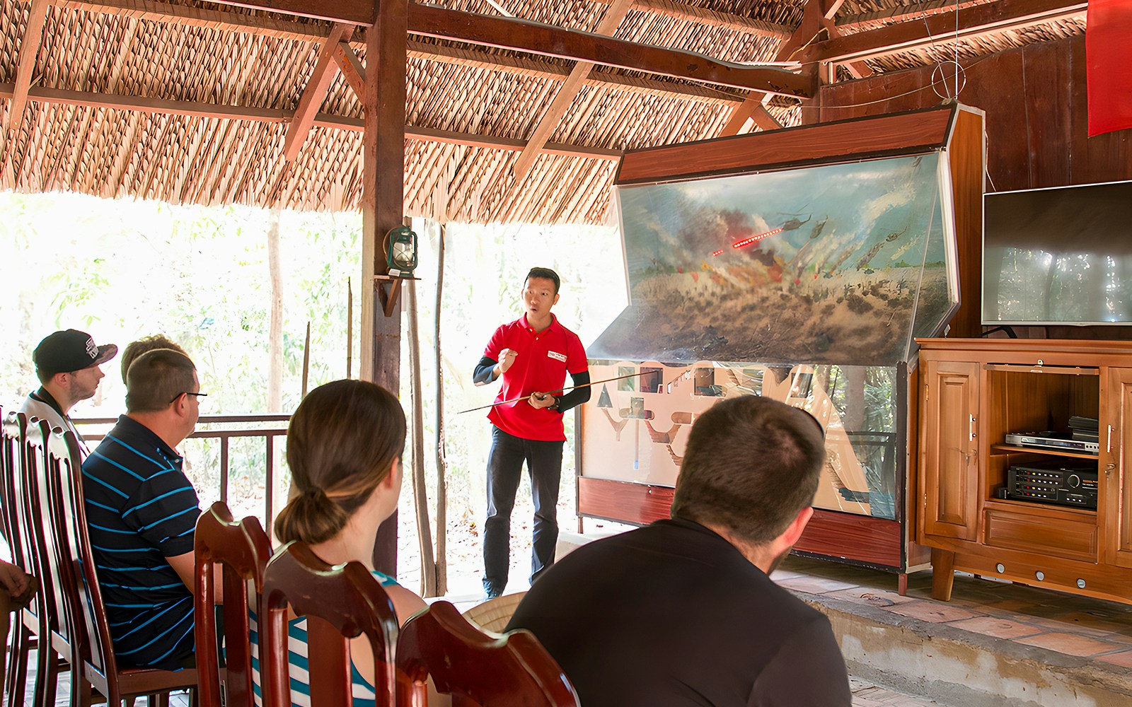 Guide explaining war strategies at Cu Chi tunnel to a group of visitors.
