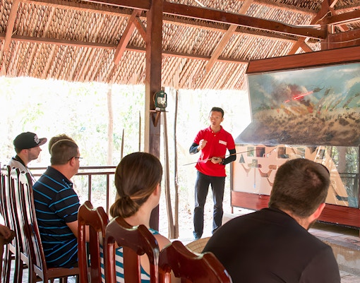 Guide explaining war strategies at Cu Chi tunnel to a group of visitors.