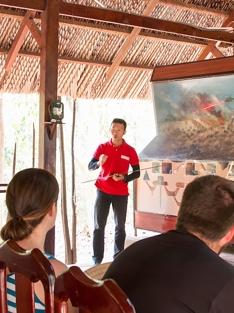 Guide explaining war strategies at Cu Chi tunnel to a group of visitors.