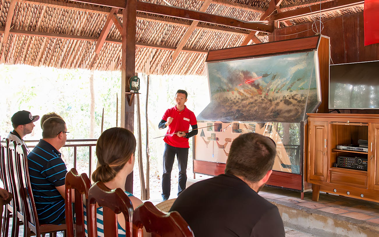 Guide explaining war strategies at Cu Chi tunnel to a group of visitors.