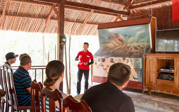 Guide explaining war strategies at Cu Chi tunnel to a group of visitors.