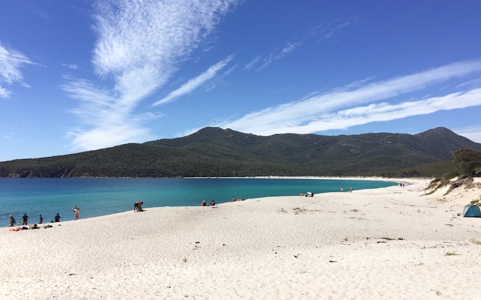 Wineglass Bay beach with visitors, turquoise water, and forested hills, Tasmania.
