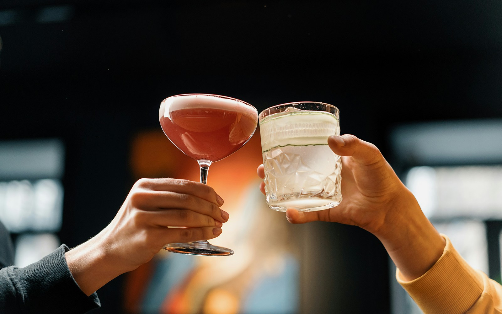 Two people toasting with cocktails in a dimly lit setting.