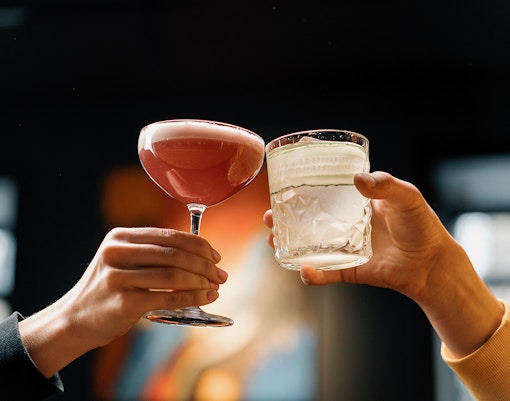 Two people toasting with cocktails in a dimly lit setting.