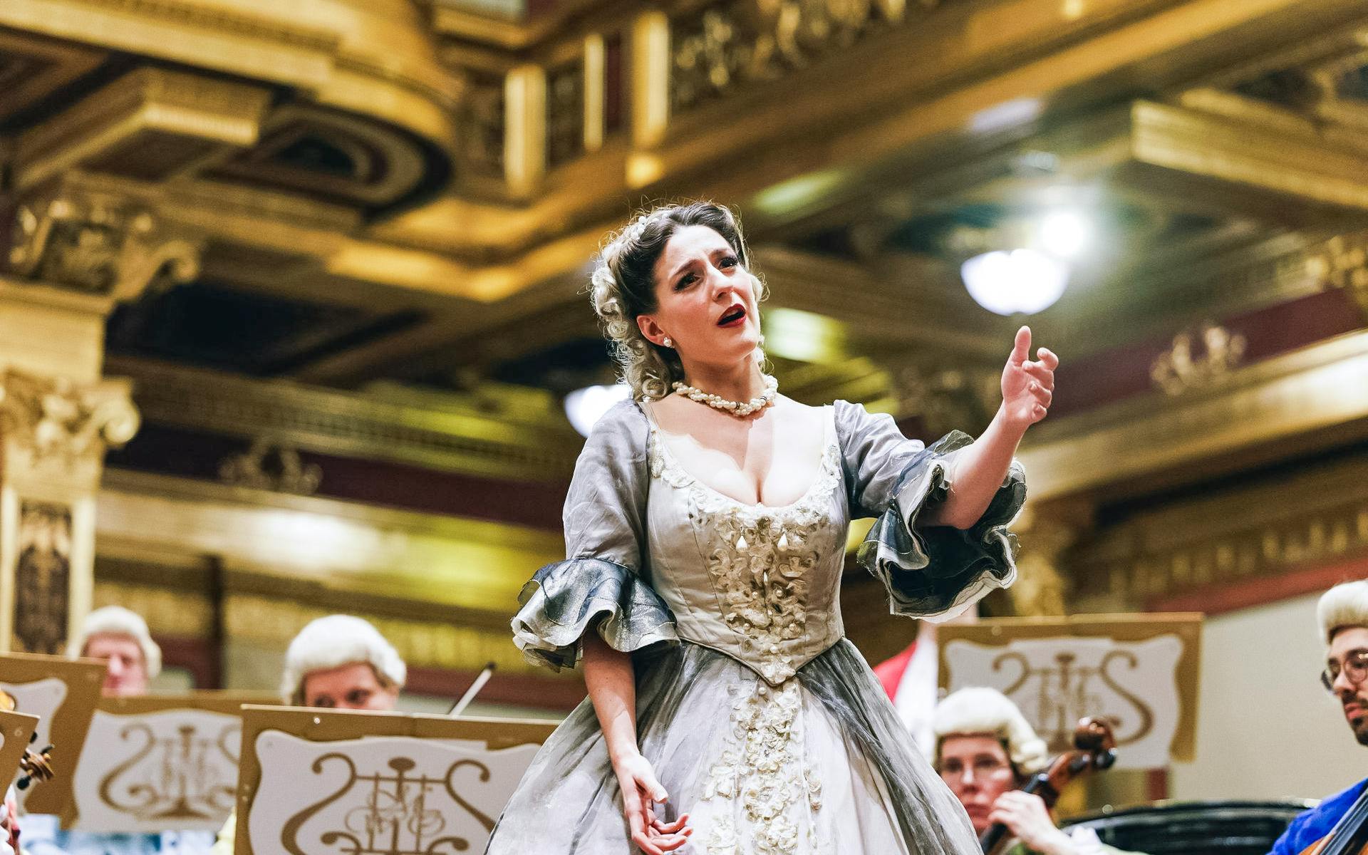 Opera singer performing with orchestra at Mozart concert in ornate concert hall.