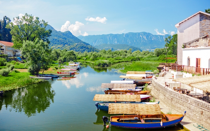 Boats docked along the shore of Lake Skadar National Park with mountains in the background.