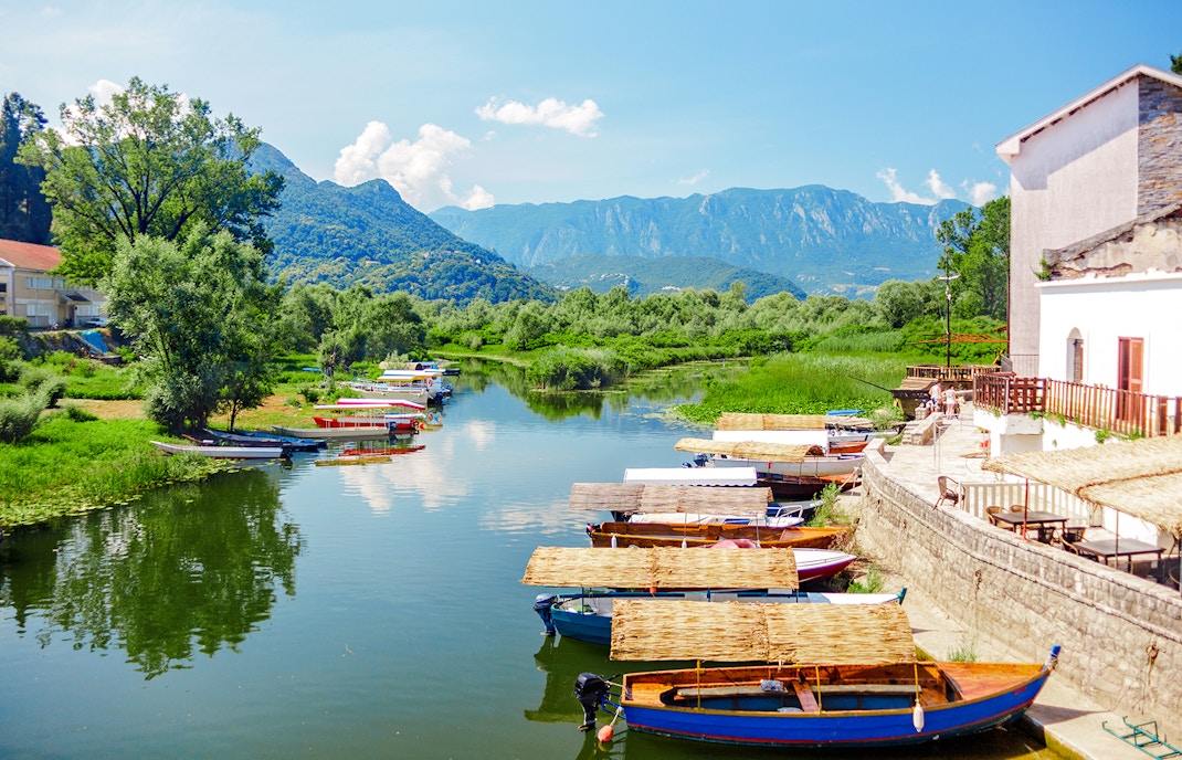 Boats docked along the shore of Lake Skadar National Park with mountains in the background.