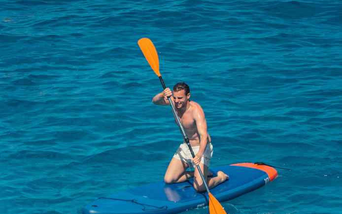 Tourist paddleboarding at Cala Bassa Beach, Ibiza, Spain.