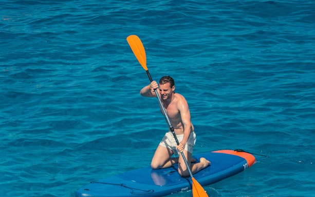 Tourist paddleboarding at Cala Bassa Beach, Ibiza, Spain.